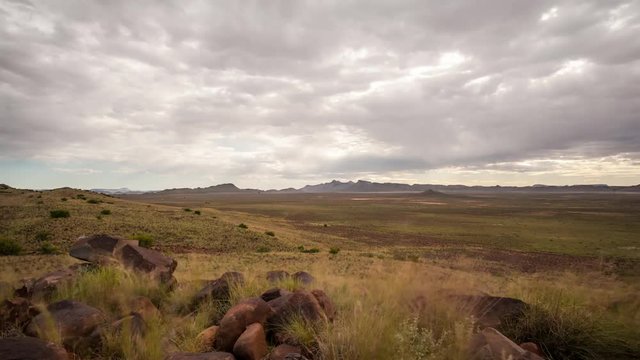 Loop of Holy grail linear timelapse showing the Karoo landscape and vistas stretched out down in the valley with a mountain in the distant background and rocks in the foreground.  Fast moving clouds blowing towards camera clearing up as it gets dark into the night with airglow in the sky available on request.