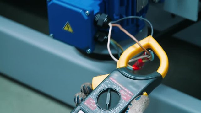 Engineer measuring technical parameters of industrial machine with tester