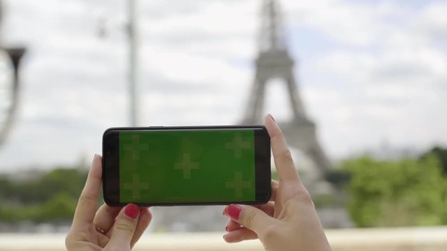 Woman using smartphone with Green Screen at Eiffel Tower, in Horizontal Landscape Mode, watching movie on touch screen with Tracking Markers. Watching Content, Videos, Blogs. Close-up.