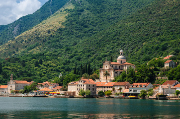 Fototapeta na wymiar View of the seaside ancient city on the Adriatic Sea shore. Houses with red-tiled roofs and an old church at the foot of the green mountain. Seascape.