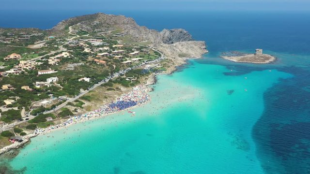 Stunning aerial view of the Spiaggia Della Pelosa (Pelosa Beach) full of colored beach umbrellas and people sunbathing and swimming in a beautiful turquoise clear water. Stintino, Sardinia, Italy.