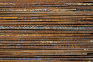Top view stack of straight old rusty high yield stress deformed reinforcement steel or iron bars. Background horizontal random pattern of deformed iron bars. 