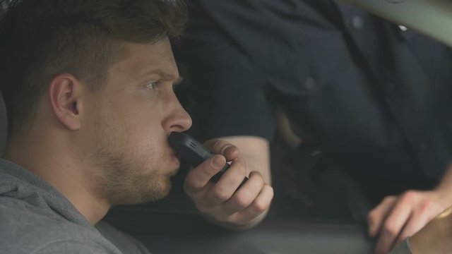 Nervous man giving policeman breath sample to check alcohol content, road safety