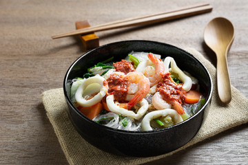 close up of seafood sukiyaki in a ceramic bowl on wooden table. asian homemade style food concept.