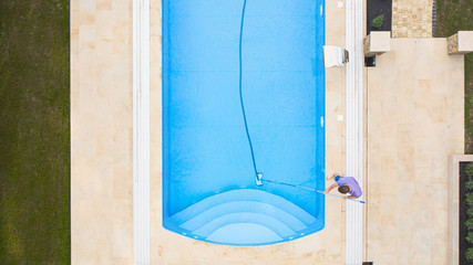 Man cleaning swimming pool with vacuum tube cleaner early