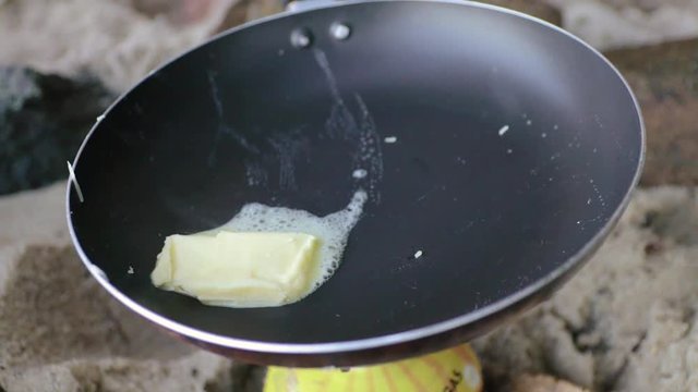 Close up of the hands of a Hispanic man with a pan melting butter during the morning in camping at the beach during a sunny day, slow motion
