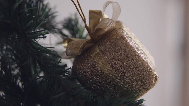 Golden bax christmas ornament hanging on dry tree branch. 4K handheld shooting.
