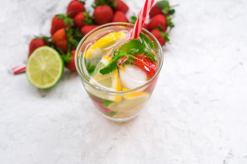 Refreshing summer alcohol drink. Ingredients: rum, soda, strawberry, mint leaves, lime and lemon. Mojito drink with strawberry on white table.