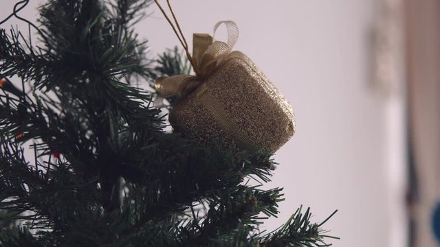 Golden bax christmas ornament hanging on dry tree branch. 4K handheld shooting.