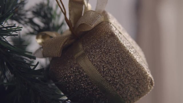 Golden bax christmas ornament hanging on dry tree branch. 4K handheld shooting.