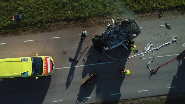 Aerial View: Rescue Team of Firefighters and Paramedics Work on a Car Crash Traffic Accident Scene. Preparing Equipment, First Aid Help. Saving Injured and Trapped People from the Vehicle. Zoom out