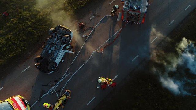 Aerial View: Rescue Team of Firefighters and Paramedics Work on a Car Crash Traffic Accident Scene. Preparing Equipment, First Aid Help. Saving Injured and Trapped People from the Burning Vehicle