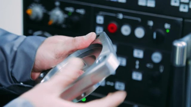 Worker holding steel part in hands. Workerman checking metal part for defects