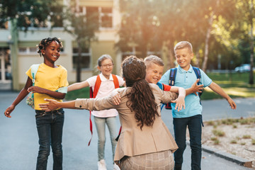 Happy children running into hug of their teacher.