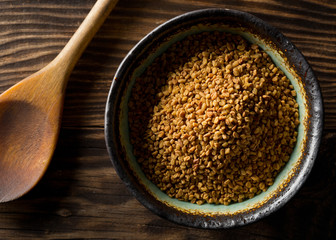 Dried, raw fenugreek seed in bowl on rustic wooden table background with spoon top view flat lay from above