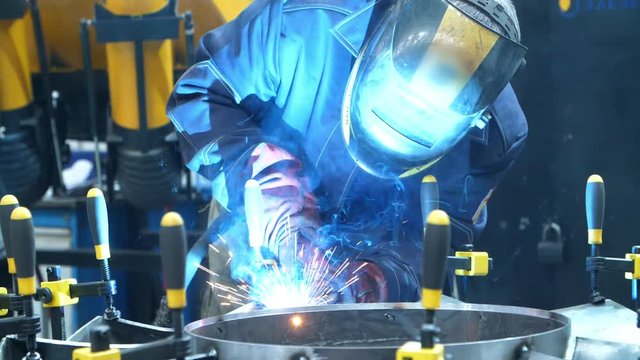 Worker in mask carrying out welding of metal billets fastened with manual clips