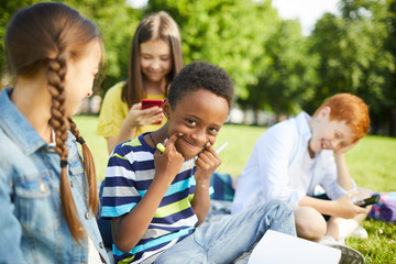 Teenage Afro-American schoolboy in striped T-shirt making funny faces while his friends laughing at him