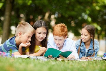 Four teenage school friends studying together in park lying on grass after classes at school