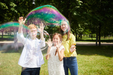 Jolly excited multi-ethnic kids in casual outfits playing with big soap bubbles together while...