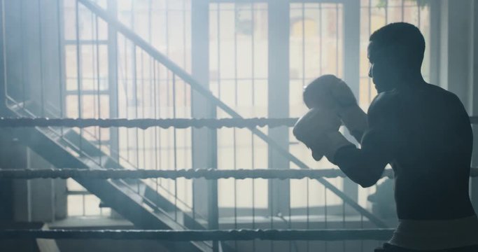 Cinematic slow motion shot of a professional young muscular shirtless african man is practicing shadow boxing work out in a ring. 
