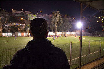 millenial boy at soccer match in the night from behind