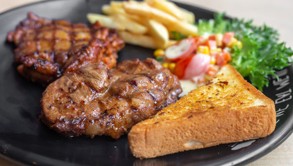 The roasted pork with buttered bread and french fried and vegetable in the dark plate in the natural light. 