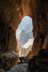 Rocky mountain range view from inside an orange-rock cave illuminated by sunlight