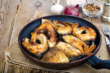 Old frying pan with fried fish on wooden table.