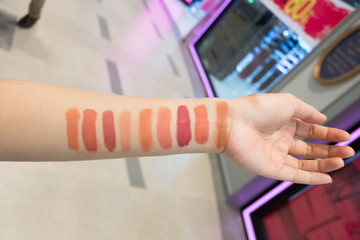 Closeup of a female buyer choosing the selected color of a lipstick trying on her skin.