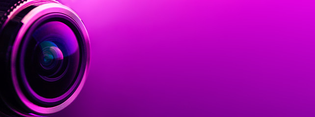 Banner. Camera lens and dark purple backlight. Side view of the lens of camera on purple background. Camera Lens Close Up. Optics