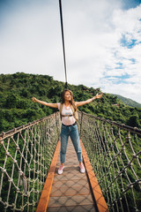 the girl raised her hands up on the suspension rope bridge over the rainforest in Yalong Bay