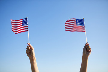 Close-up of unrecognizable people holding small American flags on sticks while watching parade devoted to independence day