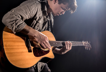 Obraz premium Guitarist, music. A young man plays an acoustic guitar on a black isolated background