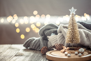 Little Christmas tree over Christmas lights bokeh in home on wooden table with sweater on a...