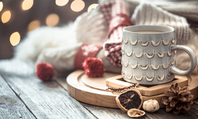 Coffee cup over Christmas lights bokeh in home on wooden table with sweater on a background and decorations. Holiday decoration