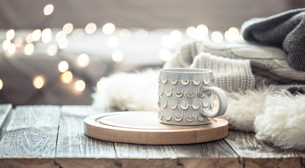Coffee cup over Christmas lights bokeh in home on wooden table with sweater on a background. Holiday decoration, magic Christmas