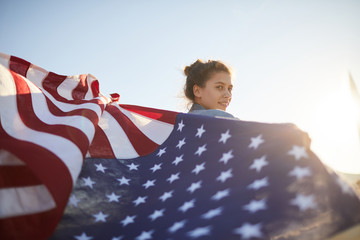 Portrait of smiling pretty young woman with hair bun holding waving flag while walking outdoors