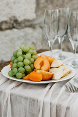 Peaches and grapes on a plate next to empty glasses for wine. Preparation for the celebration.