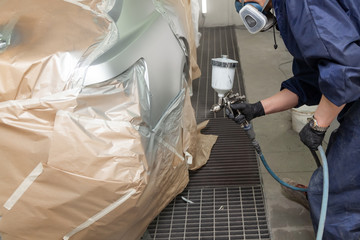 A male worker paints with a spray gun a part of the car body in silver after being damaged at an...