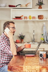 Modern bearded man using cellphone and drinking coffee with laptop.