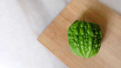 A green round hybrid bitter gourd, placed on a wooden cutting board.