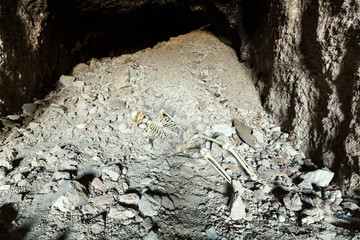 Skeleton in a dark cave in the ground lying on rocks