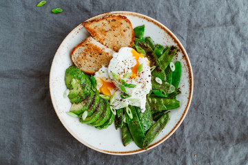 Top view of healthy breakfast or lunch. Fried snow peas, avocado, poached eggs are sprinkled chia seeds with toasts.