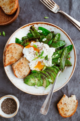 Top view of healthy breakfast or lunch. Fried snow peas, avocado, poached eggs are sprinkled chia seeds with toasts.