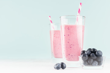 Violet fresh milk dessert with blueberries in bowl, striped straw in modern youth interior in pastel soft mint color and white wood table, copy space.