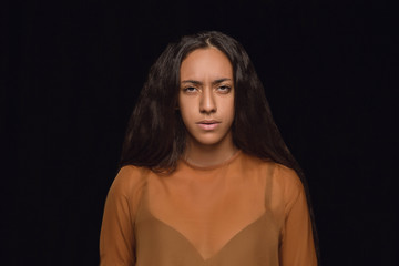 Fototapeta premium Close up portrait of young african-american woman isolated on black studio background. Photoshot of real emotions of female model. Facial expression, human nature. Sadness, look serious.