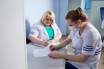 Experienced doctor fat woman and aspiring young doctor sittins at the table and discussing the medical problems