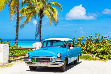 Obraz na płótnie Canvas Amerikanischer blau weisser Oldtimer parkt parkt direkt am Strand unter Palmen in Varadero Kuba - Serie Kuba Reportage