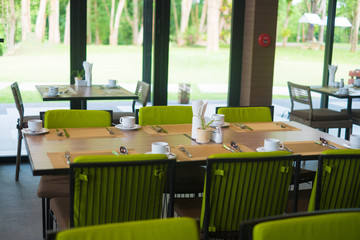 Fototapeta premium Empty restaurant part of hotel with table and armchair near windows and garden view.