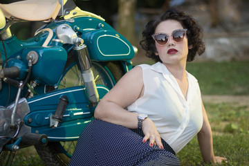 A pinup woman in a vintage dress posed next to the old motorcycle